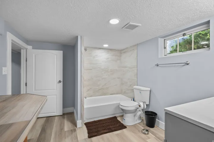 Bathroom featuring a white bathtub, light-toned wall tile, wood-finish flooring, and a window with exterior foliage