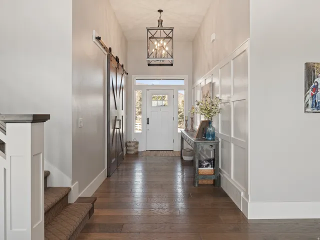 Foyer featuring wood-finish flooring, a white front door with sidelights, board and batten wall detailing, a dark bronze pendant light fixture, and a dark wood barn door
