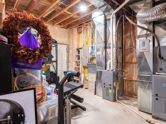 Basement mechanical room featuring exposed ductwork, a water heater, furnace units, and a concrete floor