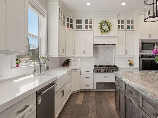Gourmet kitchen featuring extensive white cabinetry, professional-grade range with custom hood, stainless steel appliances, a large window over the sink, and wood-finish flooring