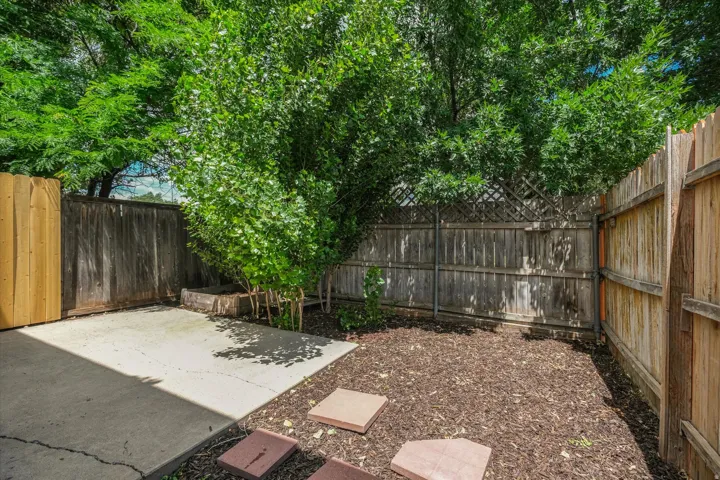 Private outdoor space featuring concrete patio, wood fencing, stepping stones, and mature trees