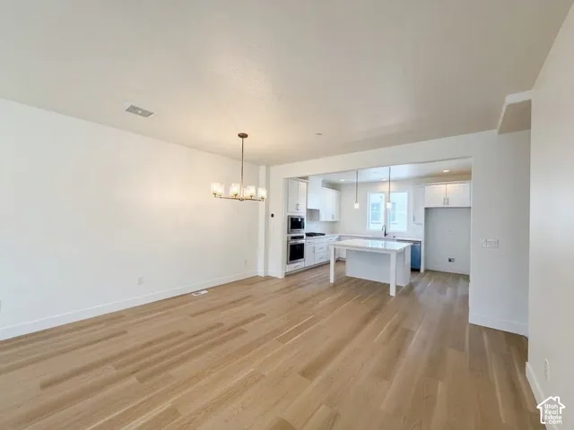 Open-concept living space featuring wood-finish flooring, a modern chandelier, and a kitchen with white cabinetry, a central island, and stainless steel appliances