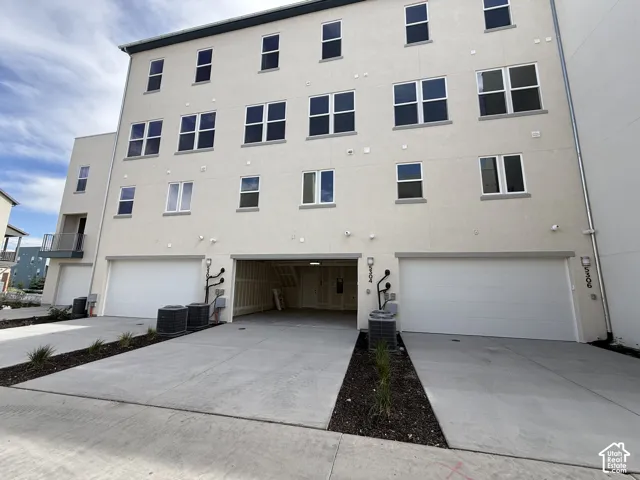 Three-story stucco exterior with multiple windows, concrete driveway, and two white garage doors