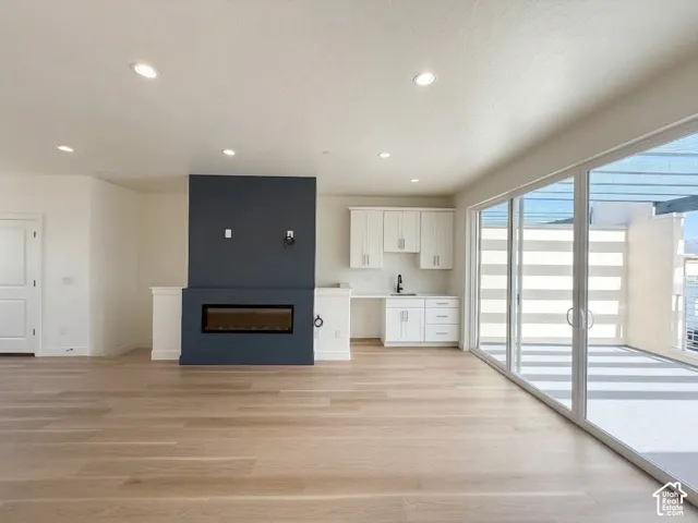 Recessed lighting, wood-finish flooring, linear fireplace with accent wall, built-in cabinetry with sink, and sliding glass doors to outdoor area