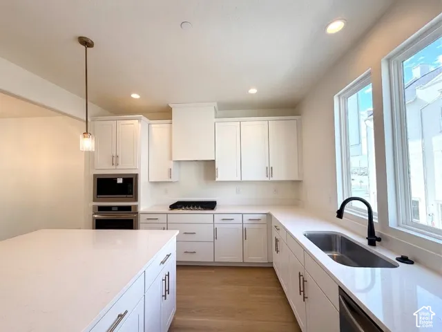 Kitchen featuring white cabinetry, light-toned countertops, a stainless steel sink with a matte black faucet, and integrated stainless steel appliances