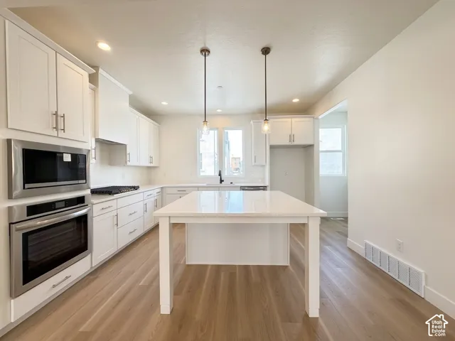 Modern kitchen with light wood-finish flooring, white cabinetry, integrated stainless steel appliances, and a central island with dual pendant lighting