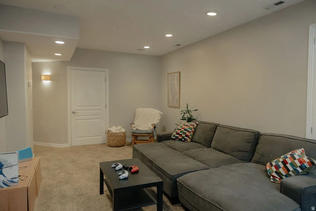 Recessed ceiling lighting illuminates a spacious room featuring neutral-toned walls, plush carpeting, and a contemporary panel door