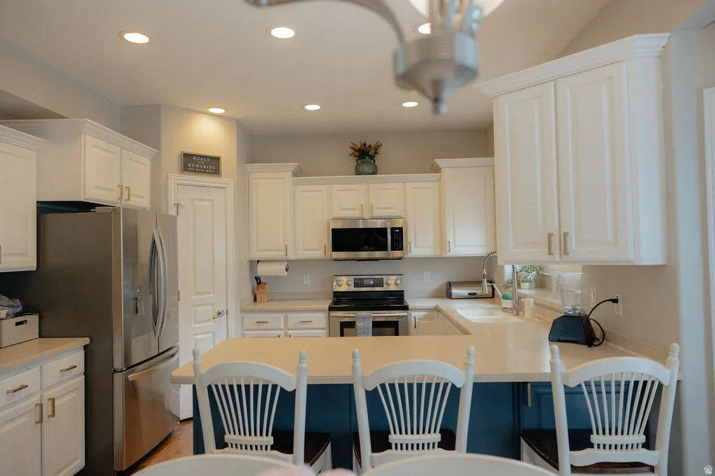Kitchen featuring white shaker-style cabinetry, recessed ceiling lighting, light-toned countertops, a stainless steel appliance suite, and a kitchen island with seating