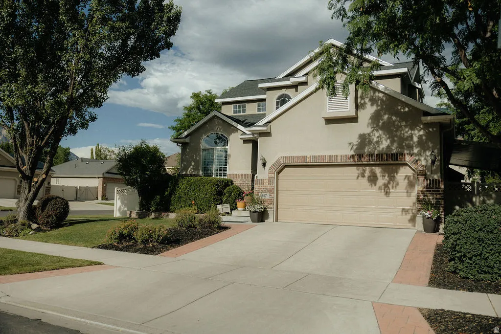 Stucco and brick facade featuring an arched garage door, concrete driveway, and established landscaping
