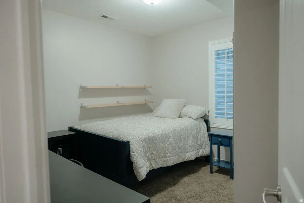 Neutral white walls frame a room featuring a window with white plantation shutters, built-in floating shelves, and carpeted flooring