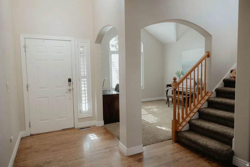 Entryway featuring wood-finish flooring, a white paneled door with sidelight and plantation shutters, and a natural wood staircase with carpeted treads