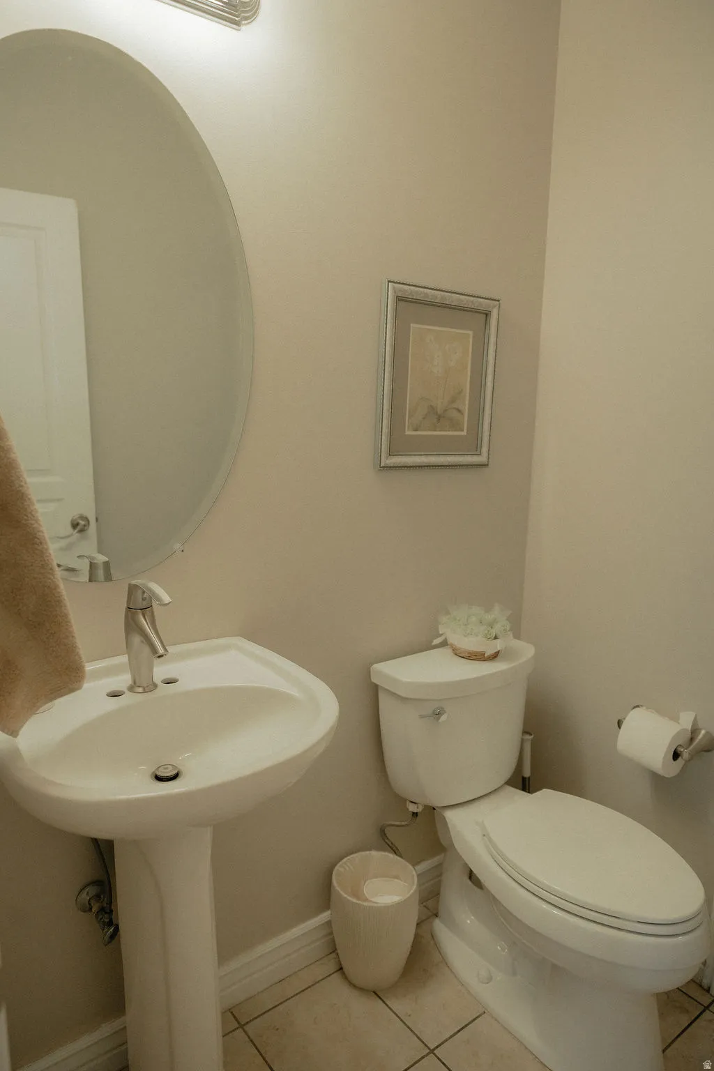 Pedestal sink with a polished chrome faucet, oval mirror, and tile flooring