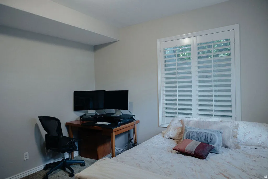 Window with white plantation shutters and white trim, set within a neutral-toned room featuring light-colored walls and a carpeted floor