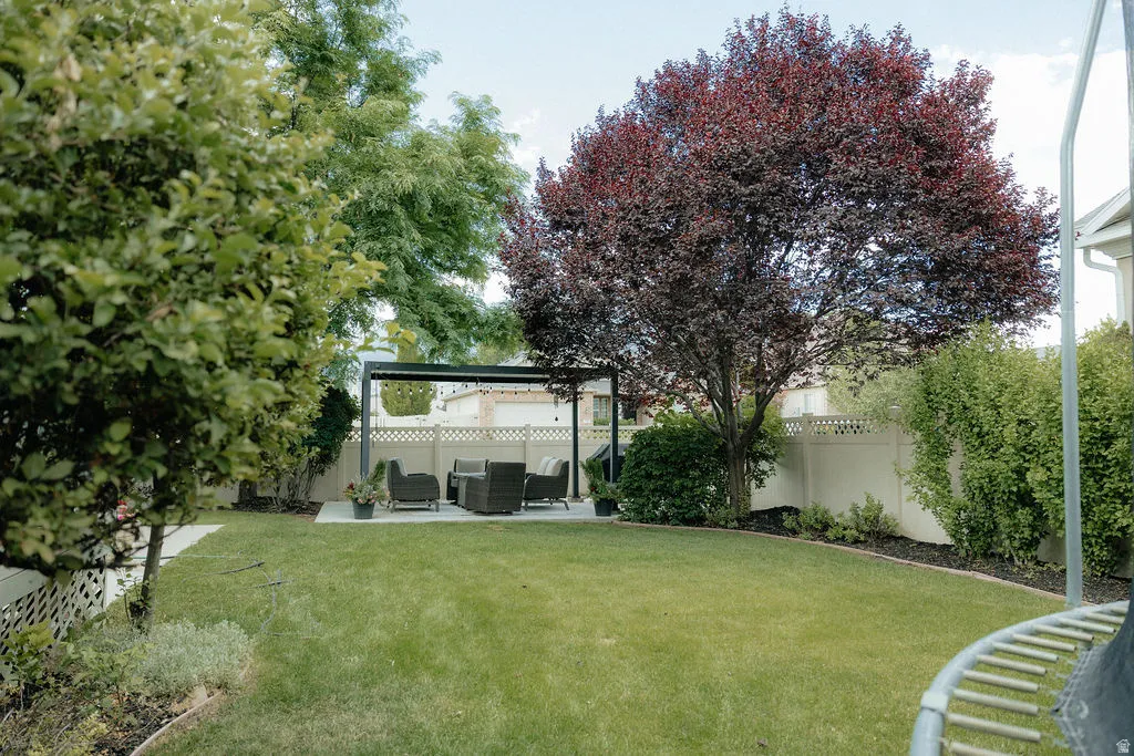 Spacious backyard featuring a manicured lawn, established trees, and a concrete patio with a modern pergola