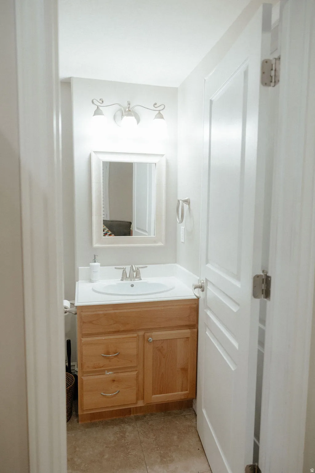 Bathroom featuring a wood-finish vanity with a white countertop and integrated sink, framed mirror, and a three-light fixture