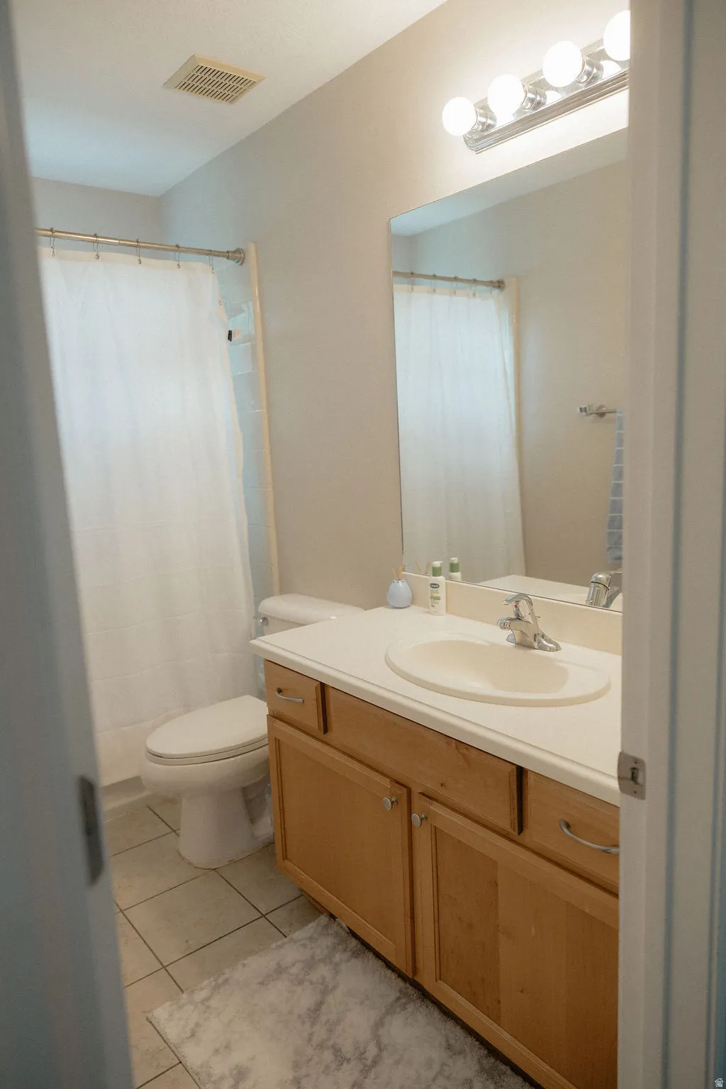 Full bathroom featuring a single vanity with wood-finish cabinetry, a large mirror, and tiled flooring