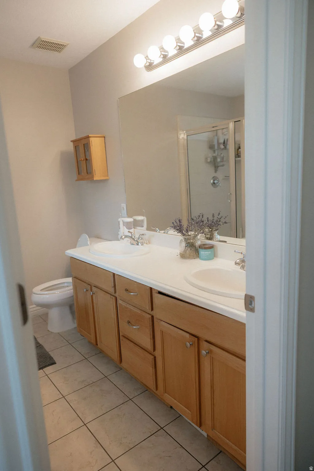Bathroom featuring a double vanity with white countertops, dual undermount sinks, and natural wood cabinetry