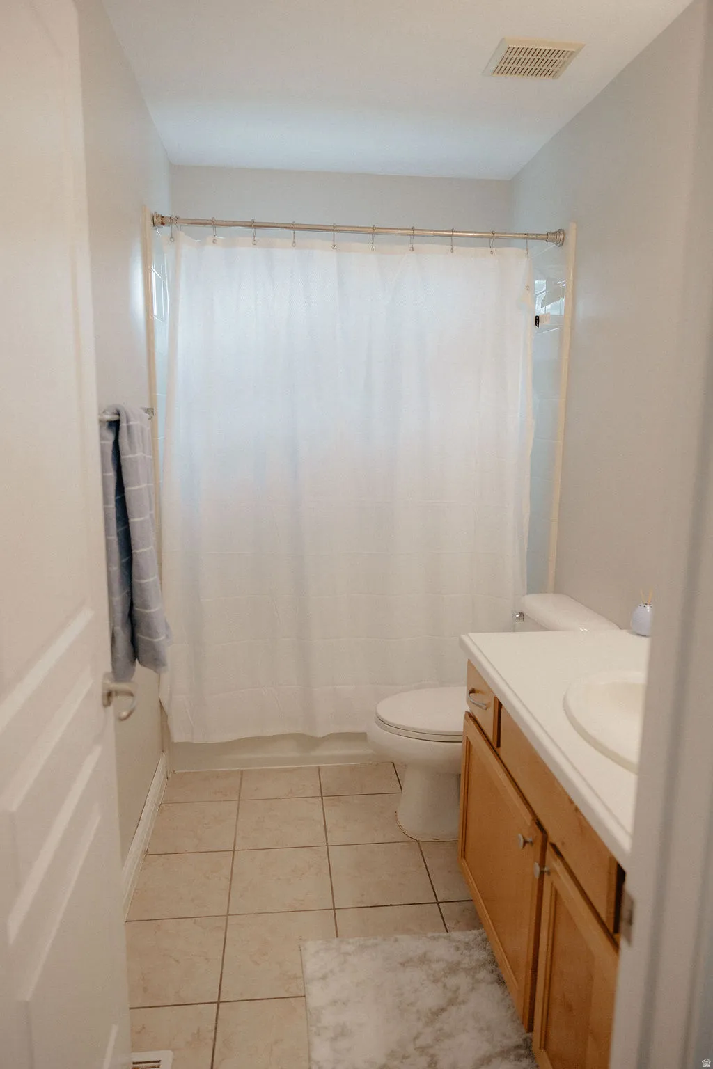 Bathroom featuring a full shower with white curtain, ceramic tile flooring, and a single vanity with wood-finish cabinetry and a solid surface countertop