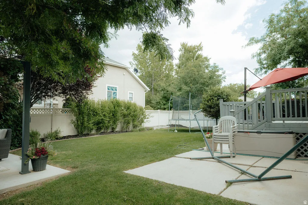 Expansive backyard featuring a manicured lawn, an elevated wood-finish deck with railings, and a concrete patio space