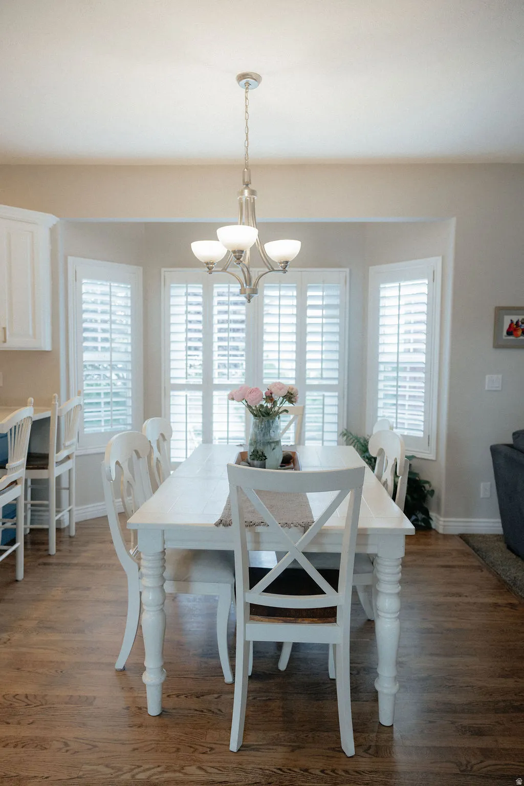 Dining area featuring wood-finish flooring, a contemporary chandelier, and a bay window with plantation shutters