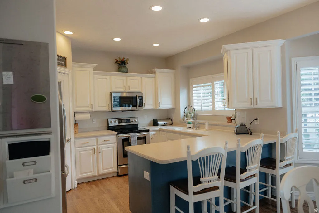 Kitchen featuring white cabinetry, stainless steel appliances, recessed lighting, and wood-finish flooring