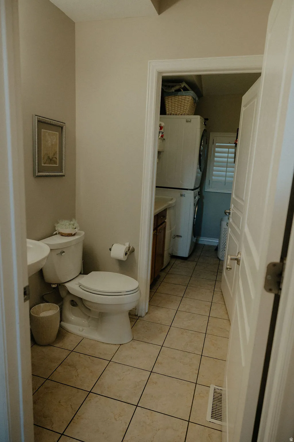 Tile flooring in a neutral tone with a toilet, pedestal sink, and white baseboards