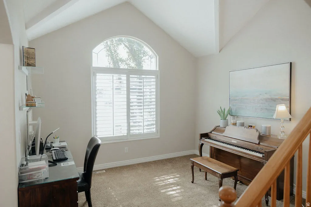 Vaulted ceiling with exposed beams, arched window with plantation shutters, neutral wall tones, and carpet flooring