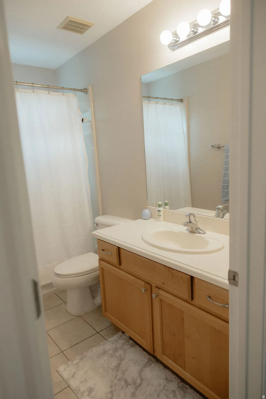 The hallway bathroom featuring a built-in vanity with wood-finish cabinetry, a single basin sink, and a light-colored countertop