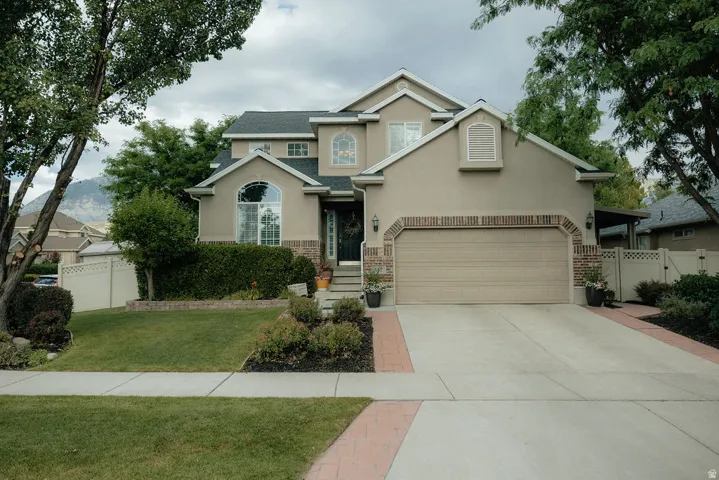 Stucco exterior featuring brick accents, a two-car garage, and a concrete driveway with brick trim