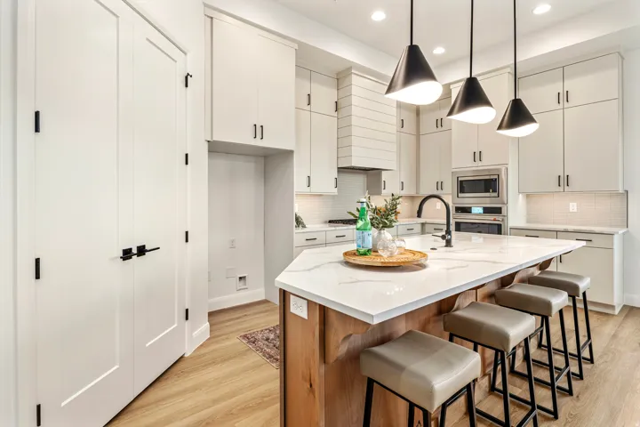 Modern kitchen featuring a large central island with seating, white shaker cabinetry, stainless steel appliances, and wood-finish flooring