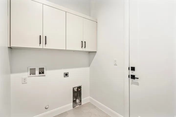 Laundry area featuring ceiling-height cabinetry with matte black hardware, white walls, and hexagonal tile flooring