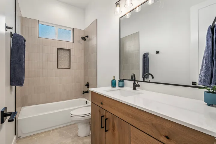 Bathroom featuring a wood-finish vanity with a white countertop and integrated sink, a rectangular mirror with a metal frame, and a shower-tub combination with vertical tile surround