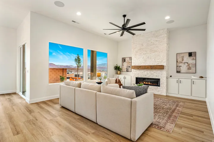 Spacious living area featuring large windows, wood-finish flooring, a contemporary linear fireplace with stone surround and wood mantel, and built-in cabinetry