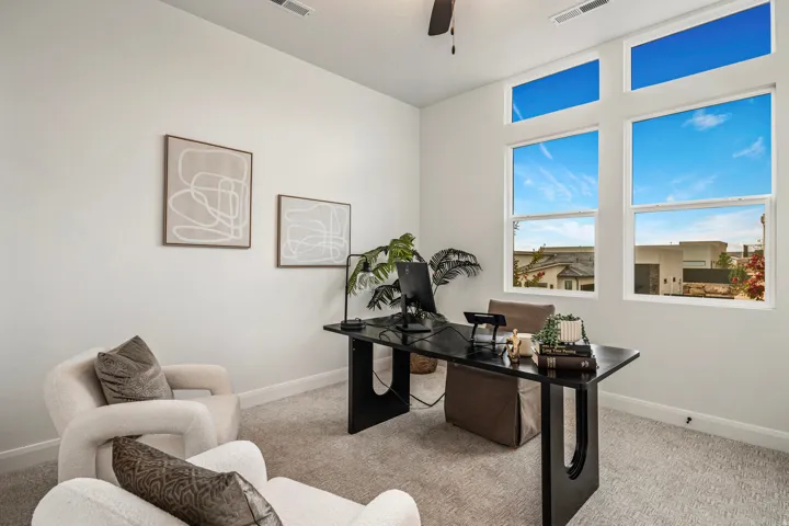 High ceilings and abundant natural light define this dedicated workspace, featuring a dark wood-finish desk and neutral carpeting