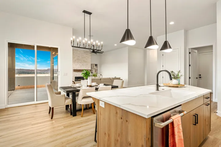 Open-concept living space featuring wood-finish flooring, a contemporary kitchen island with a white countertop and integrated sink, and an adjacent dining area with modern lighting