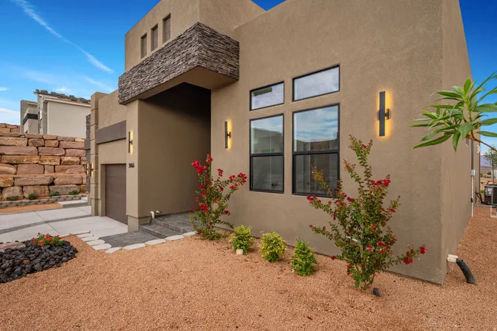 Contemporary stucco exterior featuring a stacked stone accent, modern black-framed windows, and decorative outdoor lighting