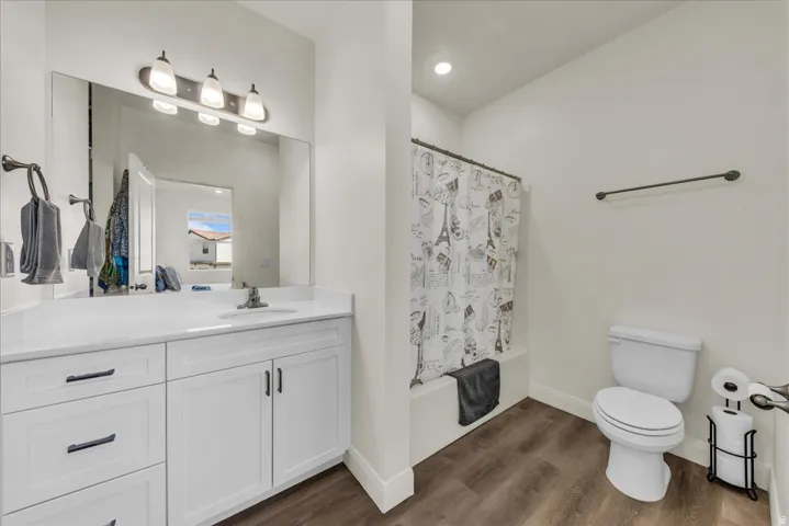 Bathroom featuring a white vanity with a light-toned countertop, a large mirror, a three-light fixture, wood-finish flooring, and a shower-over-tub combination