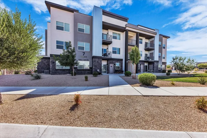 Modern multi-story building featuring contemporary architectural design, multiple private balconies, a combination of smooth stucco and stone veneer exterior finishes, and desert-friendly landscaping
