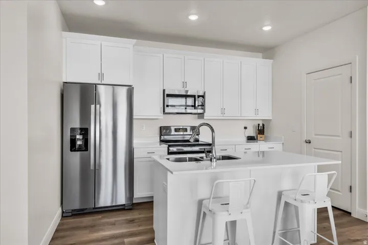 Modern kitchen featuring white shaker cabinetry, stainless steel appliances, a center island with sink, and wood-finish flooring