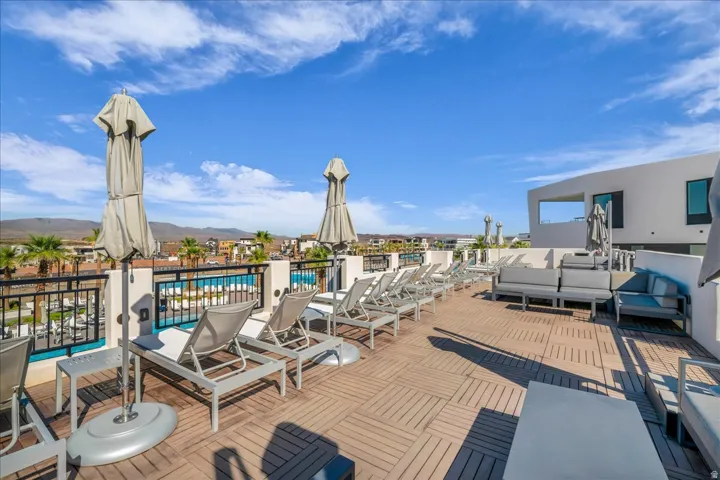 Expansive rooftop terrace featuring wood-finish flooring, a contemporary white stucco facade, and a black metal railing overlooking a pool area