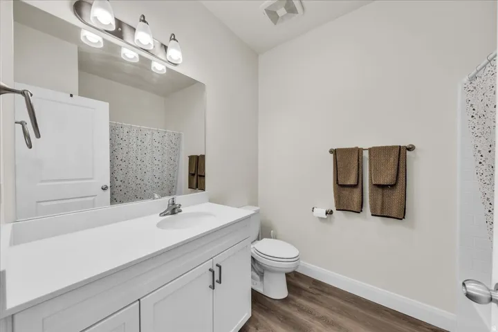 Bathroom featuring a white vanity with an integrated sink, brushed nickel faucet, large mirror, and wood-finish flooring