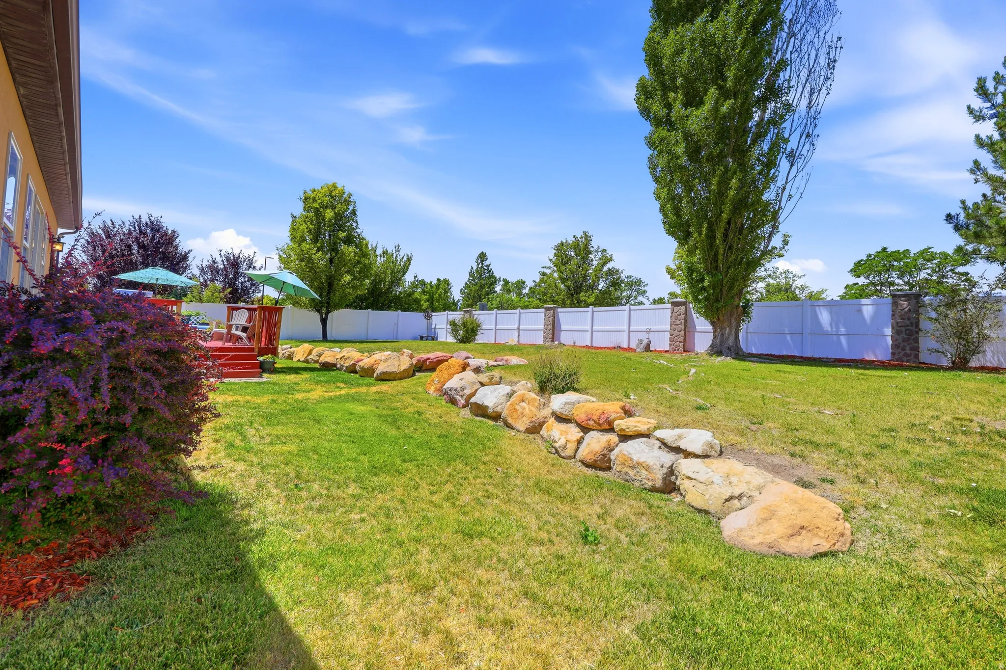 Spacious backyard featuring a multi-level red-stained wood deck, a rock retaining wall, and a full privacy fence with decorative stone pillars