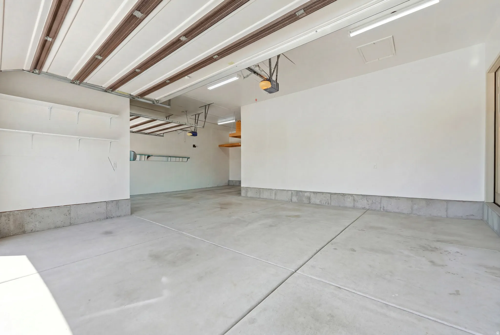 Spacious two-car garage featuring a concrete floor, built-in shelving, overhead lighting, and an automatic garage door opener