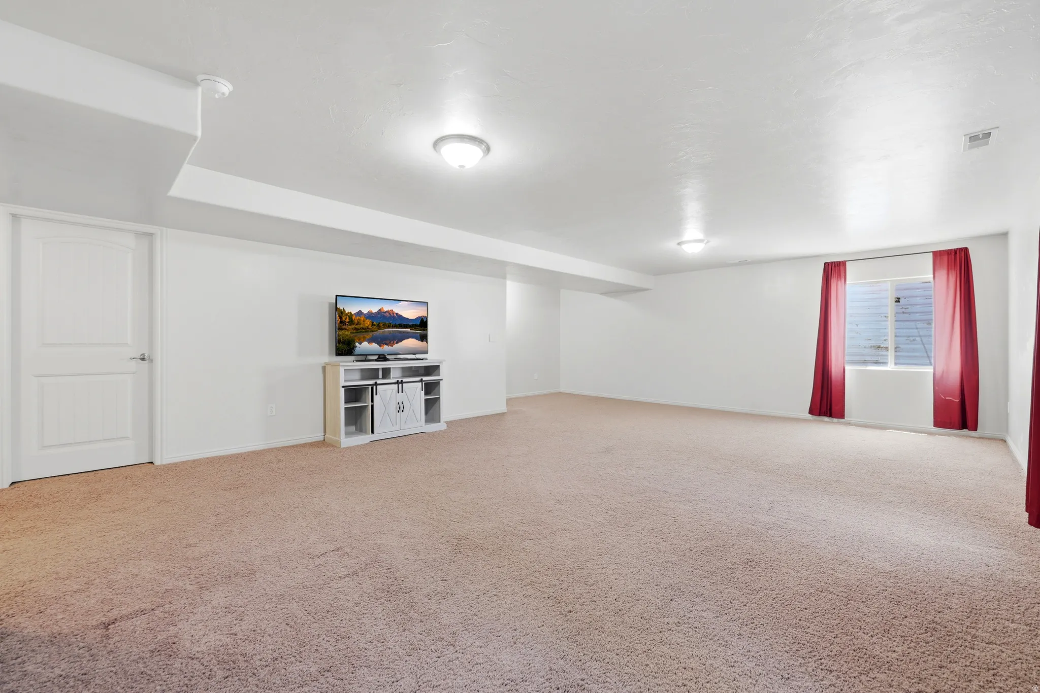 Spacious room featuring neutral carpeting, white painted walls, and ceiling-mounted flush light fixtures