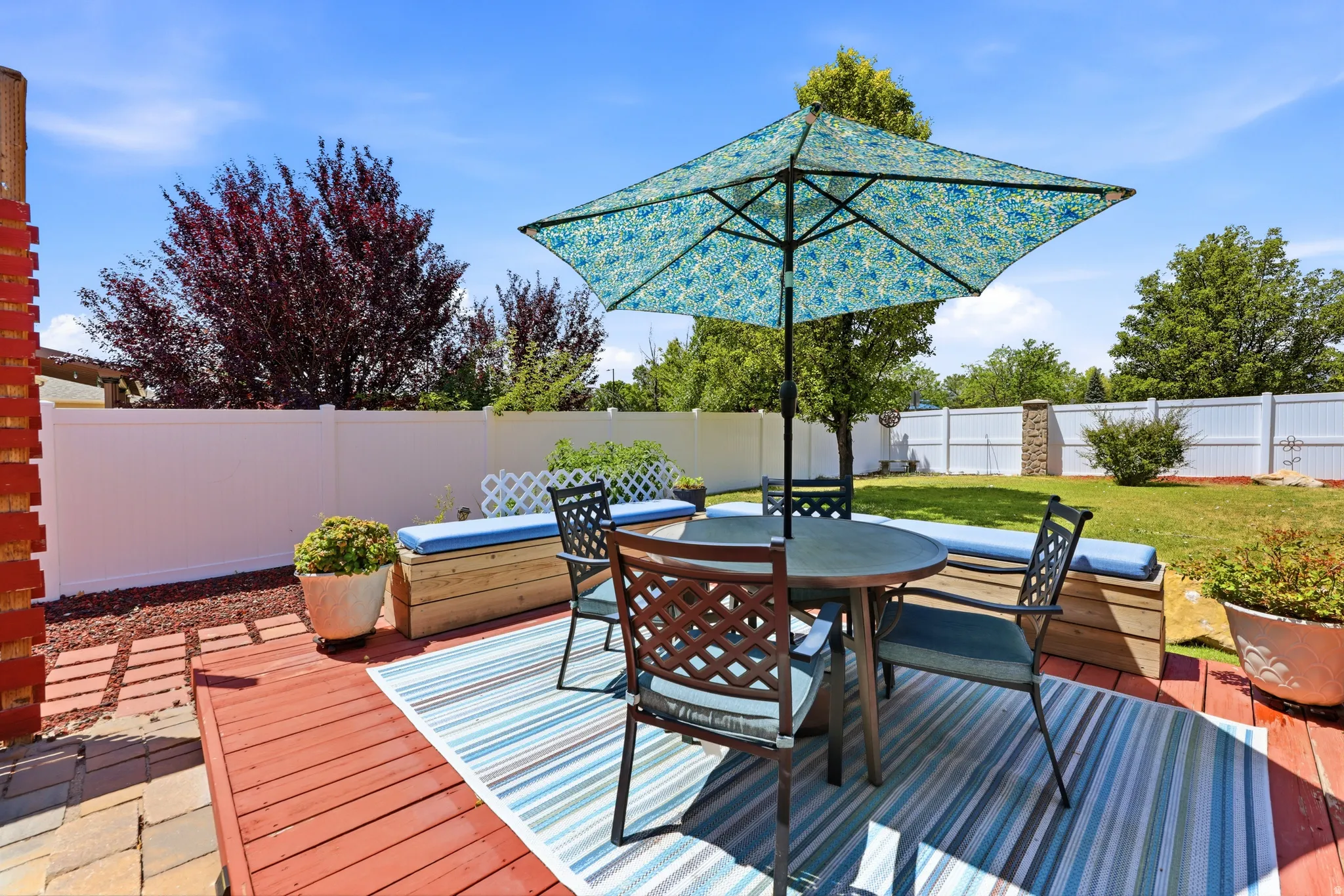 Expansive backyard featuring a red-stained wood deck, white privacy fencing, and a manicured lawn
