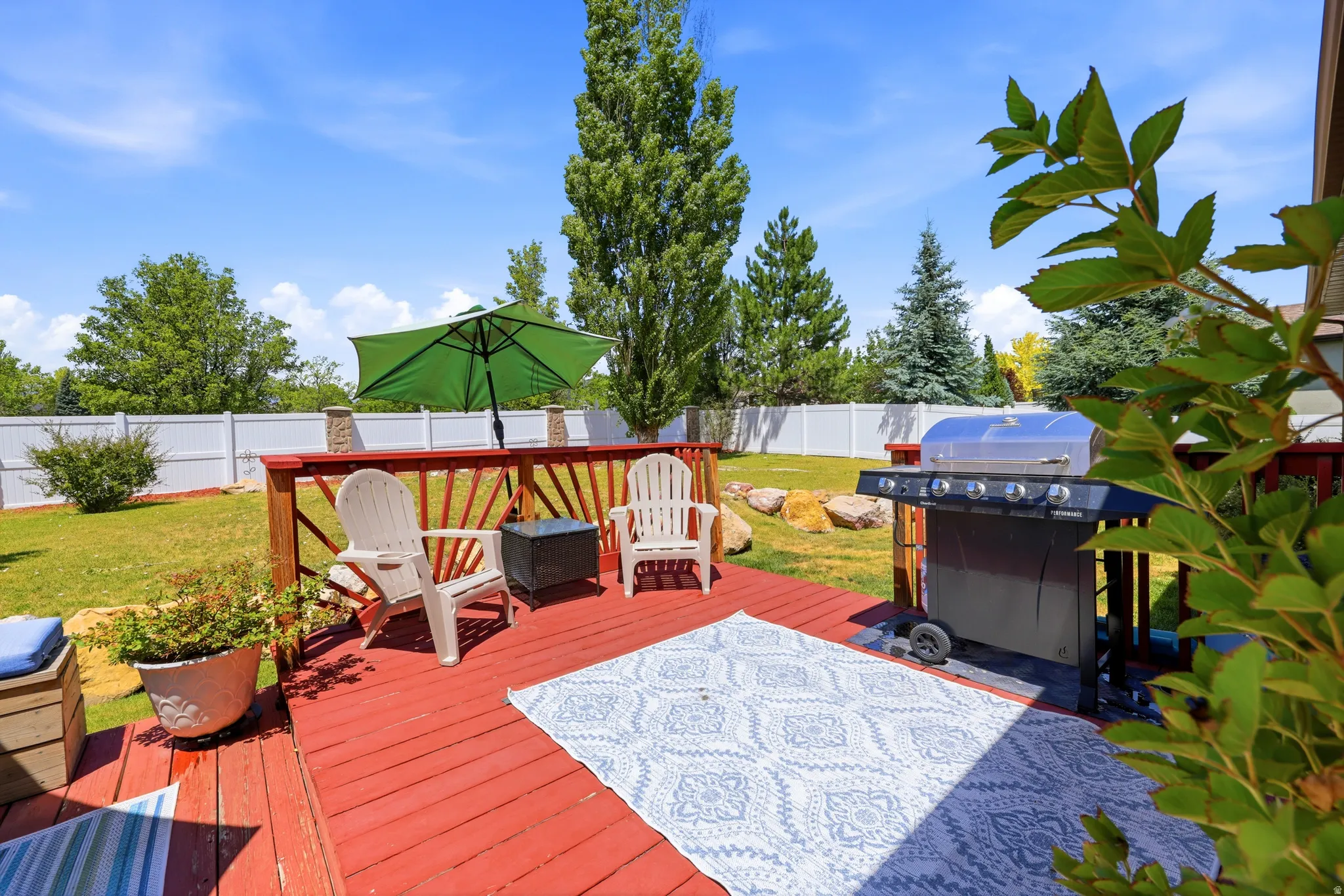 Red-stained wood deck featuring a white privacy fence and a spacious green lawn