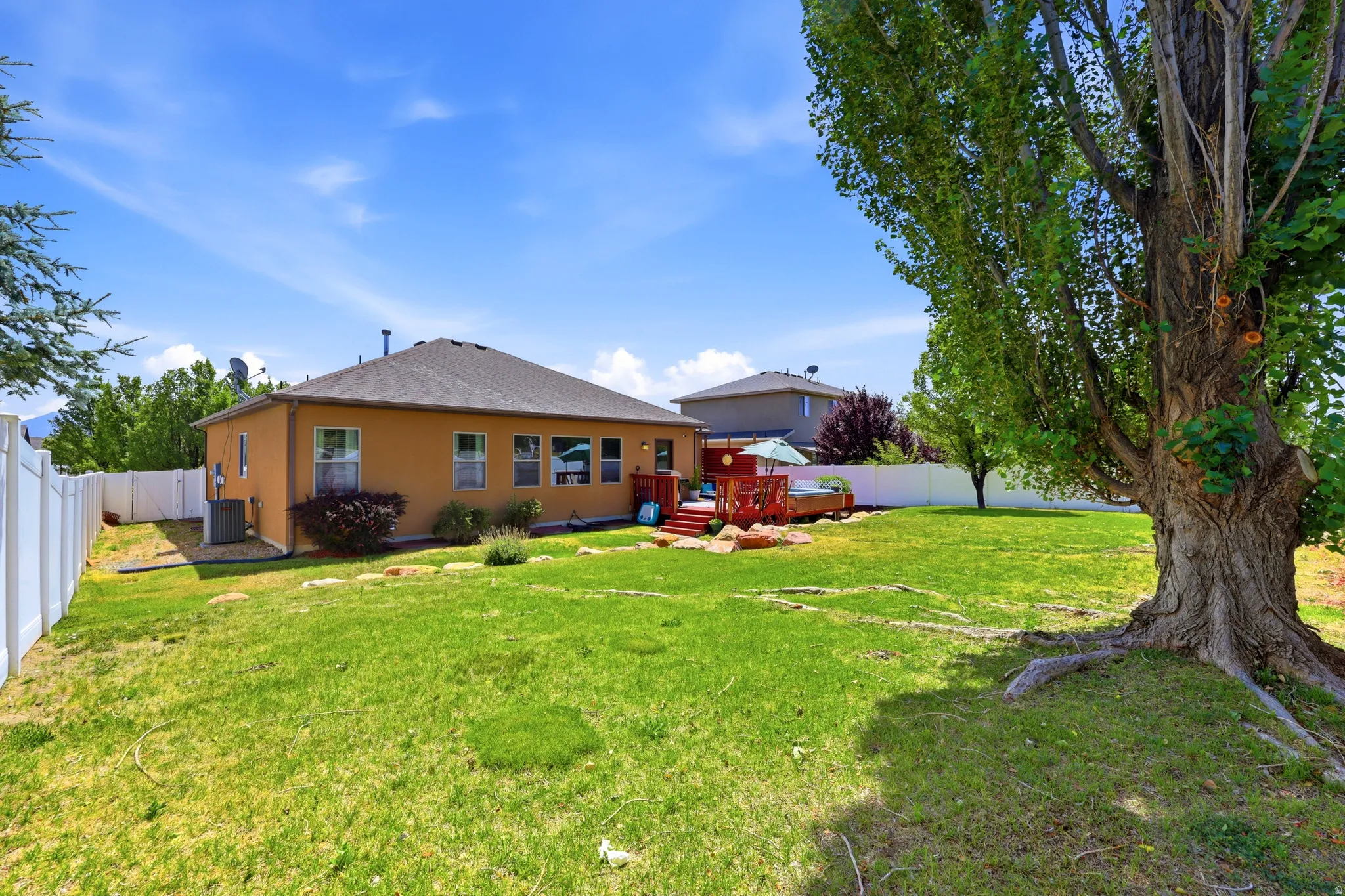 Expansive lawn area featuring a large mature tree, a privacy fence, and a multi-level deck with red-stained wood