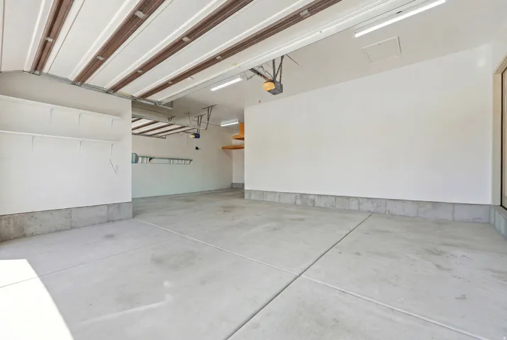 Spacious two-car garage featuring a concrete floor, built-in shelving, overhead lighting, and an automatic garage door opener