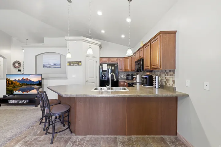Kitchen island with integrated sink, pendant lighting, wood-finish cabinetry, black appliances, and a tiled backsplash
