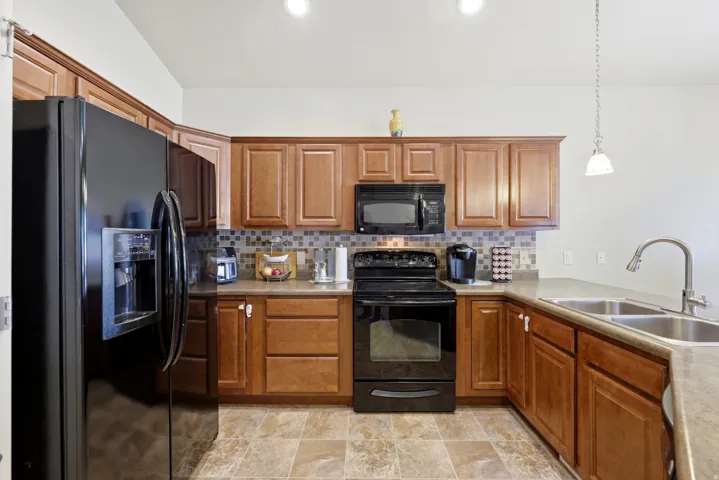 Well-appointed kitchen featuring wood cabinetry, black appliances, mosaic tile backsplash, and a double basin stainless steel sink